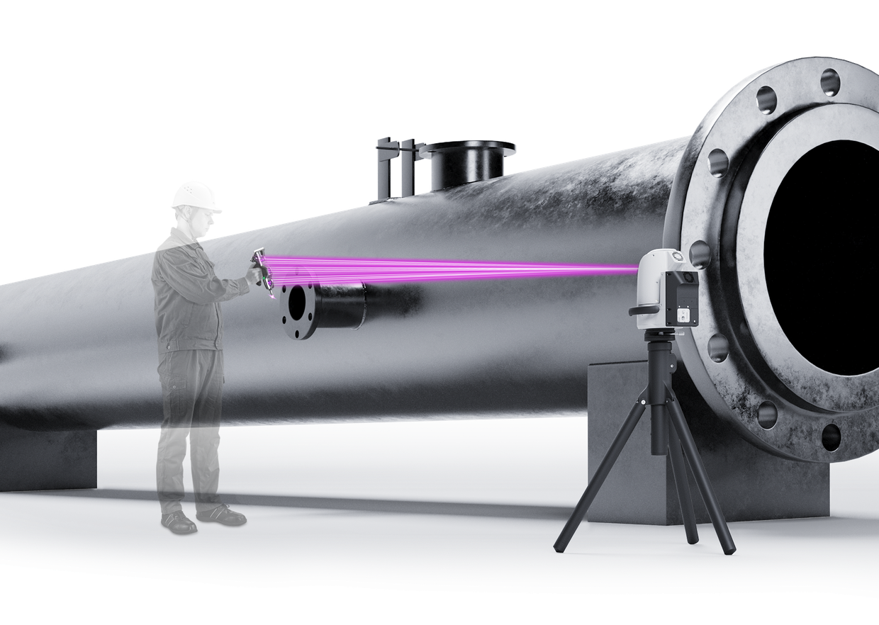 An operator touches a large pipe with the probe while the camera on a tripod follows it.