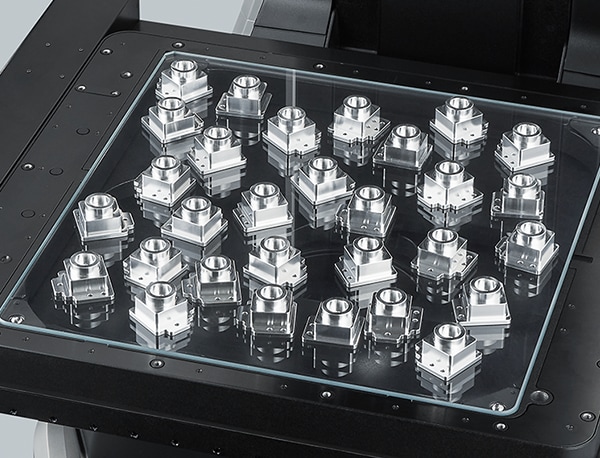 Dozens of identical parts are placed together under the glass stage to be measured in a single operation.