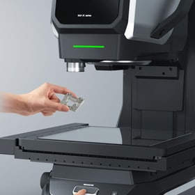 A hand places a small part anywhere on the stage without aligning it to specific coordinates.