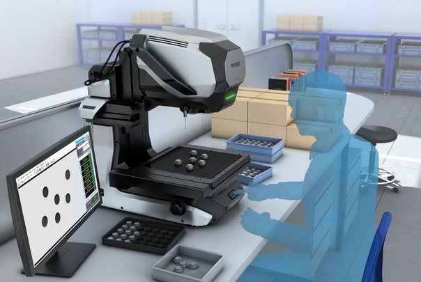 The measuring microscope in an incoming-inspection area with stacked boxes and bins, measuring a plate with 5 round holes shown on the monitor.