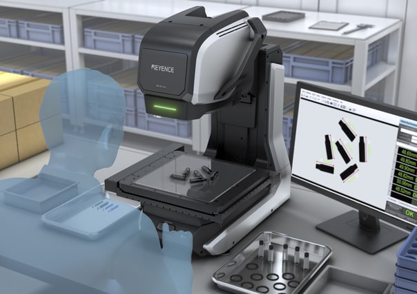 The measuring microscope in a pre-shipping area with boxes and parts trays, the monitor showing several parts with dimension readouts.
